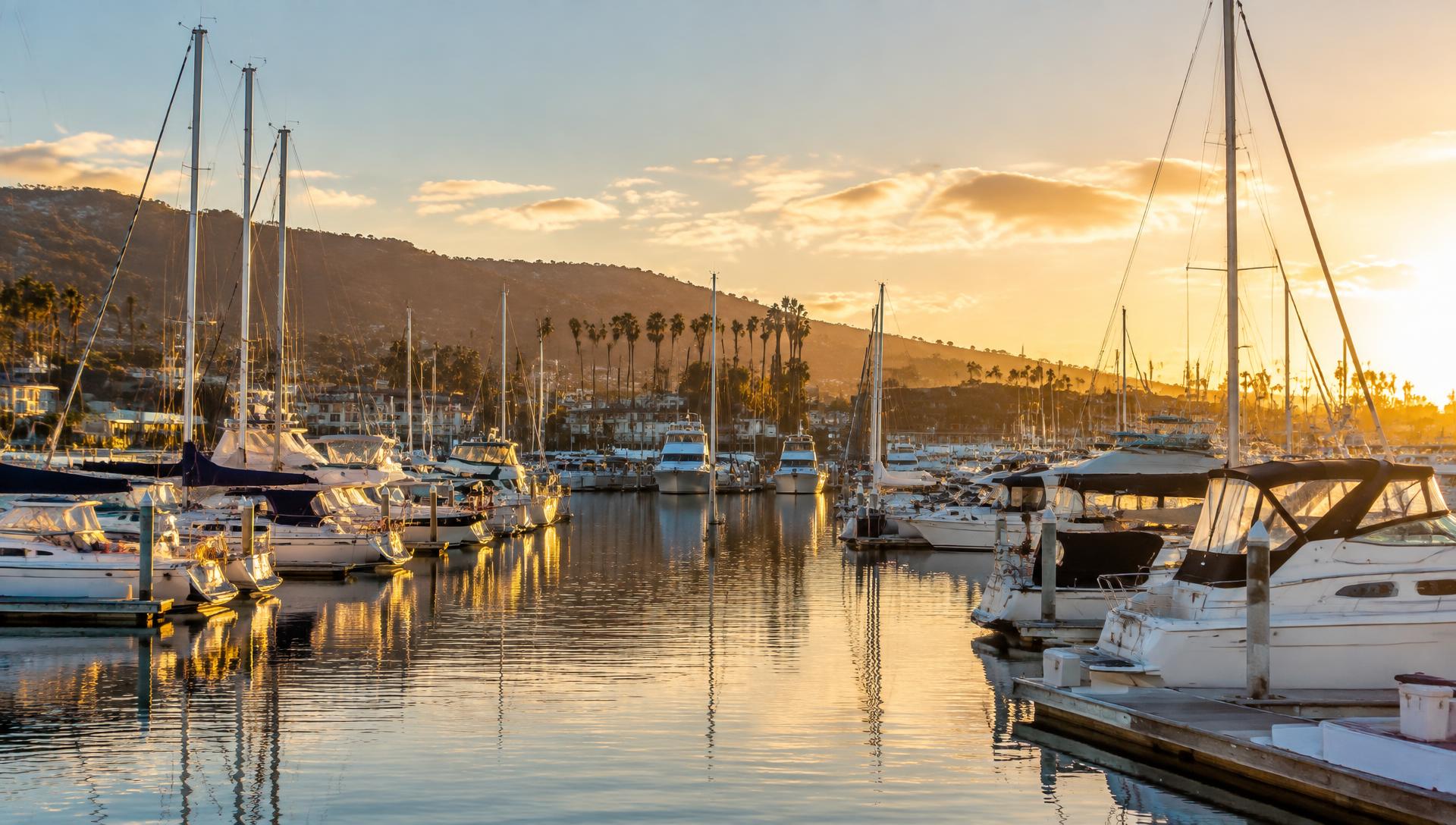 Sailboats and yachts docked at a California marina at sunset